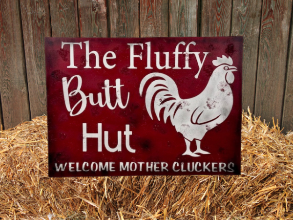 rustic sign with a red sawdust-textured background, featuring a chicken illustration and the text 'Fluffy Butt Hut - Welcome Mother Cluckers'