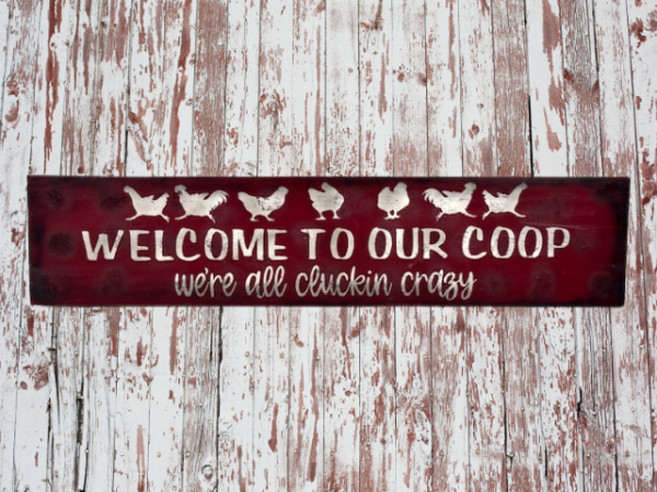 farmhouse chicken sign that has a deep red sawdust textured background with white chickens that reads Welcome to Our Coop, we're all cluckin crazy