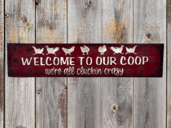 farmhouse chicken sign that has a deep red sawdust textured background with white chickens that reads Welcome to Our Coop, we're all cluckin crazy