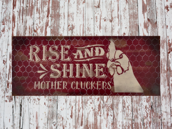 distressed and rustic red background sign with silver chicken wire - signs reads Rise and Shine Mother Cluckers