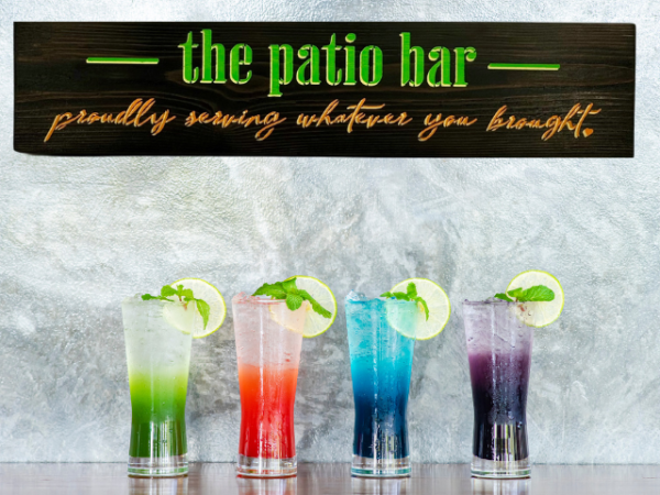 colorful lime green, orange, and yellow sign that reads "the patio bar - proudly serving whatever you brought"