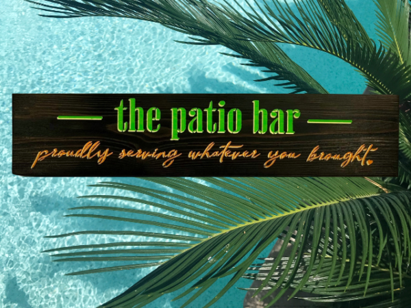 colorful lime green, orange, and yellow sign that reads "the patio bar - proudly serving whatever you brought"