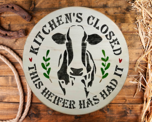 round pine wood sign that reads Kitchen's Closed - This Heifer Has Had It - with a black and white cow in the center of the round and words around the cow