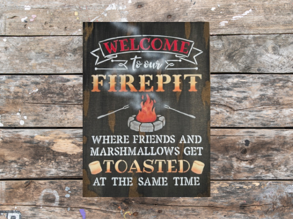 rustic campfire sign that reads "Welcome to our Firepit in beautiful orange and yellow ombre letters - the phrase "where friends and marshmallows get toasted at the same time" are painted at the bottom