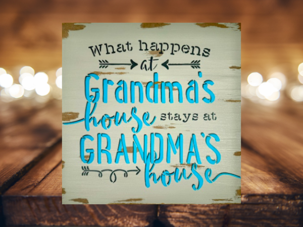 grandma's sign with a distressed mushroom gray background that says "what happens at grandma's house stays at grandma's house in teal lettering outlined in dark gray