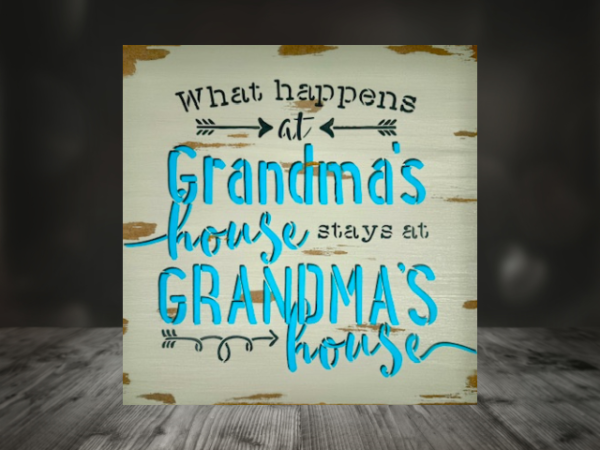 grandma's sign with a distressed mushroom gray background that says "what happens at grandma's house stays at grandma's house in teal lettering outlined in dark gray