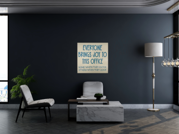 a humorous workspace sign with a dark brown background and cream colored letters that reads "Everyone Brings Joy To This Office - Some When They Enter, Others When They Leave