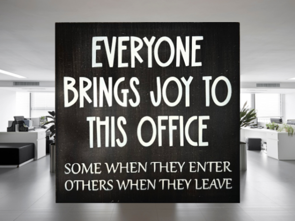 a humorous workspace sign with a dark brown background and cream colored letters that reads "Everyone Brings Joy To This Office - Some When They Enter, Others When They Leave