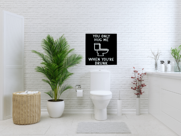 humorous bathroom sign with a black background and white wording that reads "You Only Hug Me When You're Drunk" featuring a toilet in the middle of the sign